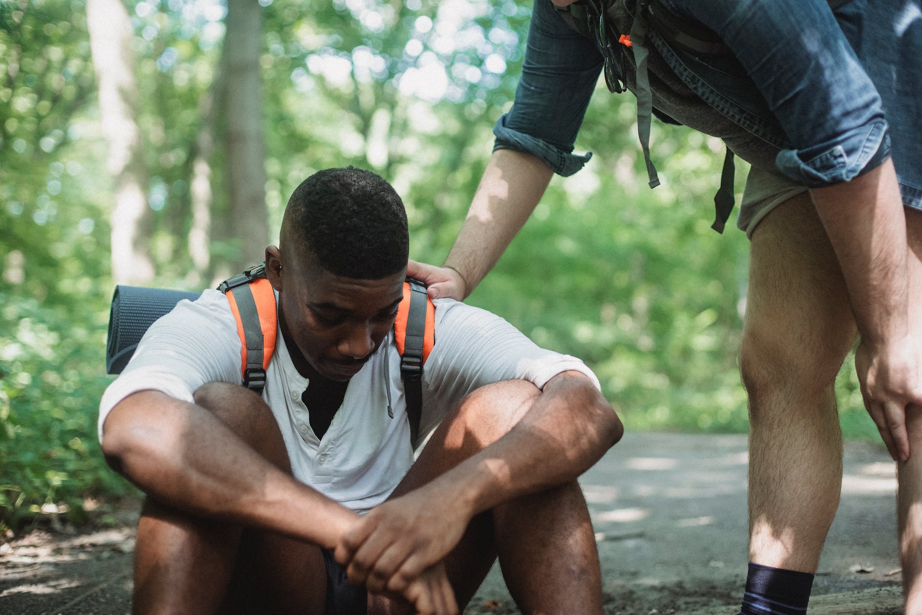unhappy black hiker sitting on ground in forest