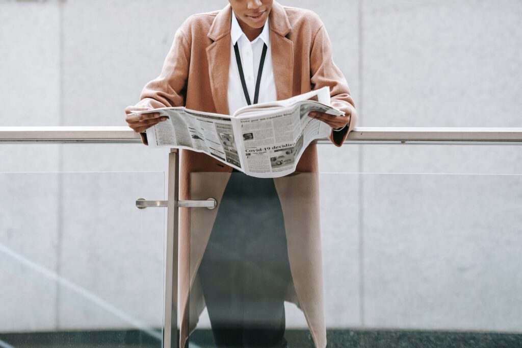 crop black businesswoman reading newspaper near modern building
