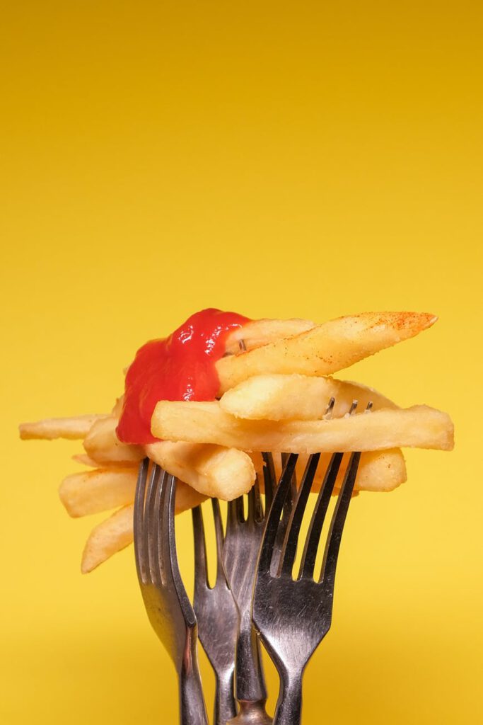 forks with fried potatoes with ketchup on yellow background