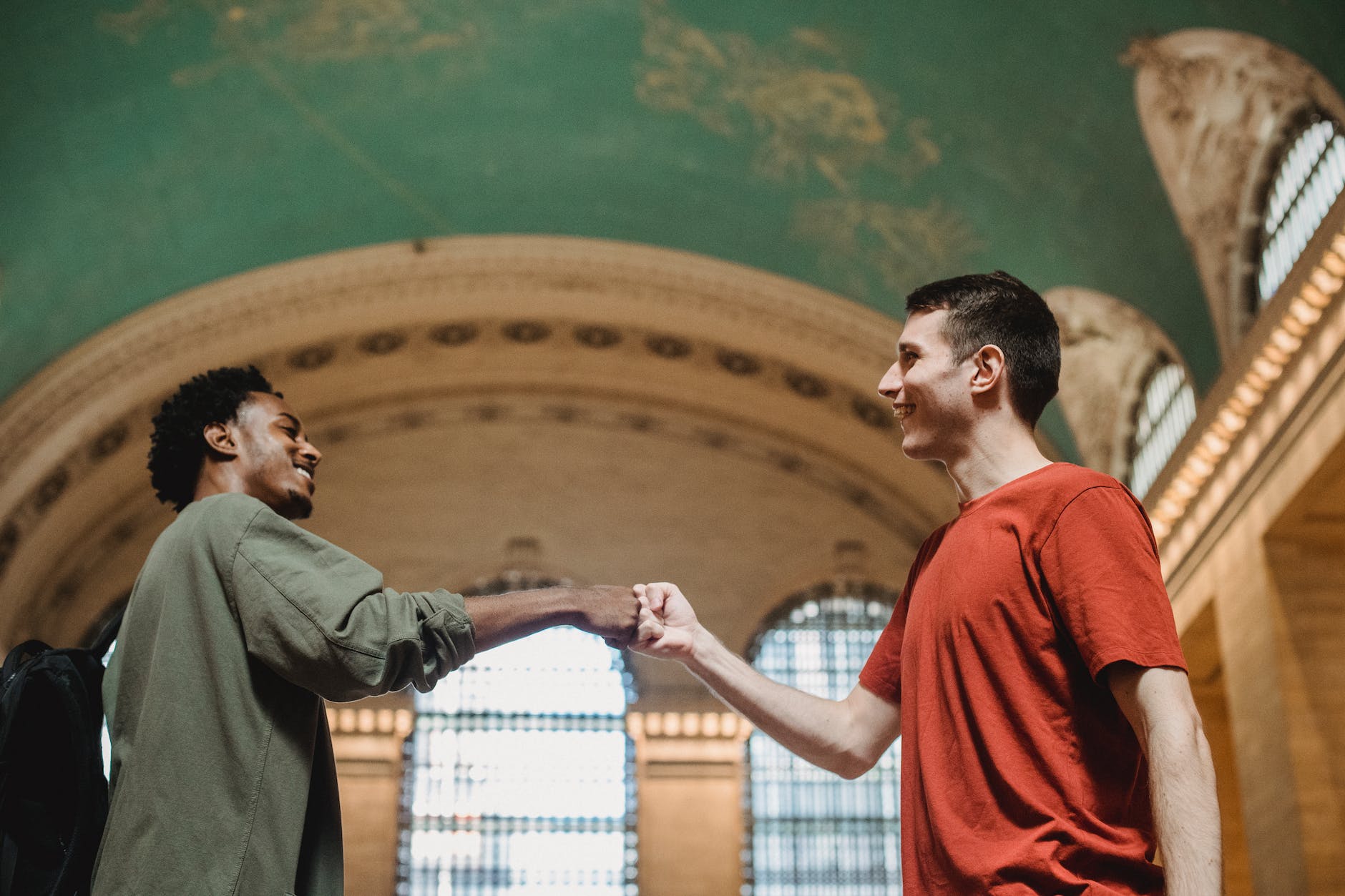 cheerful young multiracial male friends bumping fists in old building